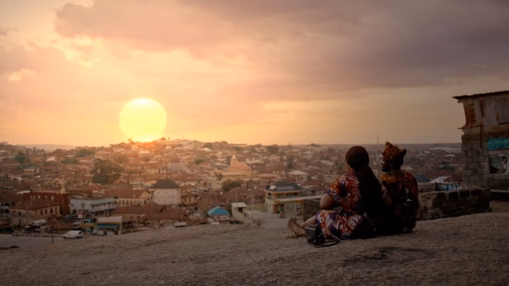 Couple sits on a cliff in a village and looks out onto the sunset